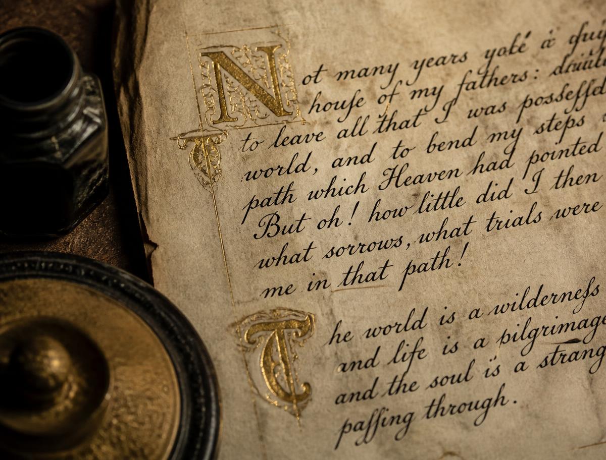 Aged parchment with black ink calligraphy and gold illuminated capitals beside an inkwell